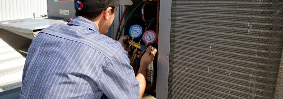 HVAC technician servicing a condenser unit in Evans